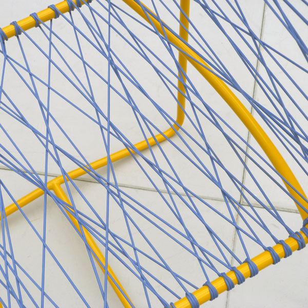 Close up of yellow metal framed chair with blue elastic criss crossed across frame to make seat and back